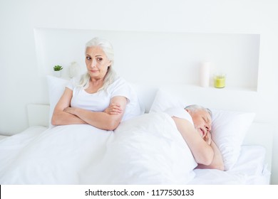 Relax, rest, retired, concept. Upset, dissatisfied woman looks aside with her hands crossed on the chest lie in a soft  linen, sheets bed near sleeping husband in bright white room interior - Powered by Shutterstock