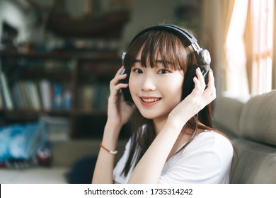 Relax And Stay At Home For New Normal Concept. Happy Asian Teenager Woman Listen Music Via Internet Streaming With Headphone. Living Room Background With Window Light.