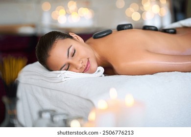 Relax, woman and hot stone massage at salon for peace, aromatherapy and stress relief at luxury resort. Back, rocks and calm person at spa for body treatment, detox and healing for health with bokeh