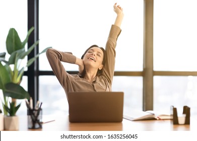 Relax At Work. Happy Young Woman Sitting In Office With A Laptop, Stretching Her Arms Above Her Head And Smiling