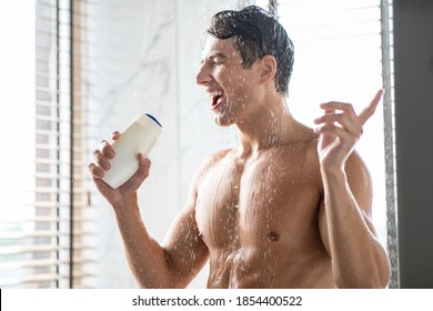 Relax. Young Man Singing In Shower Holding Shampoo Bottle Like A Microphone, Having Fun Bathing Standing In Modern Bathroom At Home. Hygiene And Male Bodycare Beauty Routine Concept.