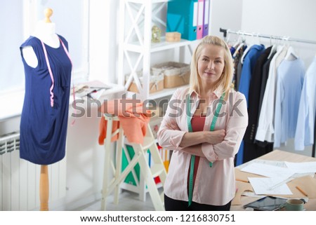 Relaxation after successful work. Unusual foreshortening from the top. Beautiful European woman looking at the camera, standing near the table in the workshop with clothes hanging in the background