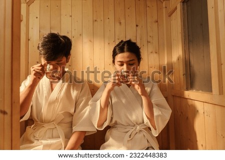 Relaxation Asian couple in bathrobe drinking hot tea while relaxing in the sauna. Healthcare and spa treatment concept.