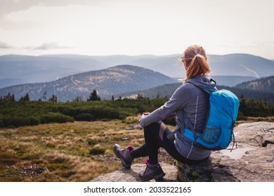 Relaxation During Mountain Hike. Woman With Backpack Sitting On Rock And Enjoying Scenic View. Tourist Hiking And Climbing At Mountain Peak