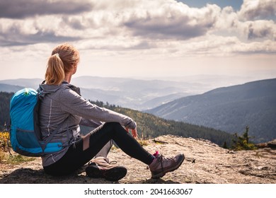 Relaxation During Mountain Trek. Woman With Backpack Sitting On Rock And Enjoying Scenic View. Tourist Hiking And Climbing At Mountain Peak