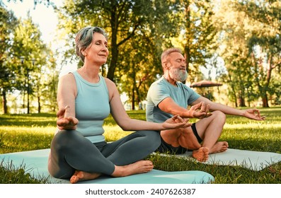 Relaxation during outdoors yoga. Calm elderly couple meditating together in lotus position under morning sun at summer park. Caucasian man and woman keeping eyes closed and hands in mudra gesture. - Powered by Shutterstock