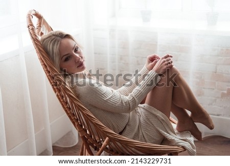 Relaxation and harmony. The girl is resting in a wicker chair and dreaming by the window.