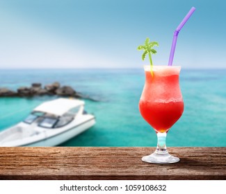 Relaxation in Summer Holiday Concept. Glass of Red Juice on Wooden Table. Blurred Sea Beach with Speed Boat as background