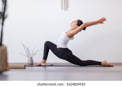 Relaxe Harmonious Beautiful Brunette Woman Yoga Instructor Standing In Anjaneyasana Pose, Horse Rider Exercise On Wooden Floor At Workout In White Yogi Classroom. Health And Spirit Improvement Concept