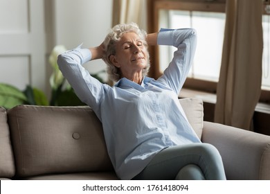 Relaxed 55s woman leaned on couch daydreaming in living room at home. No stress, enjoy fresh conditioned air, modern flat, maintain inner balance and harmony, healthy carefree comfortable life concept - Shutterstock ID 1761418094