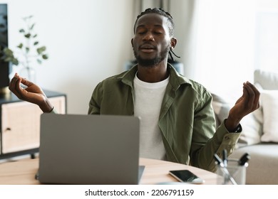 Relaxed African American Male Freelancer Meditating While Working At Laptop, Calming Down, Sitting With Closed Eyes At Workplace At Home. Online Yoga, Relaxation And Mindfulness