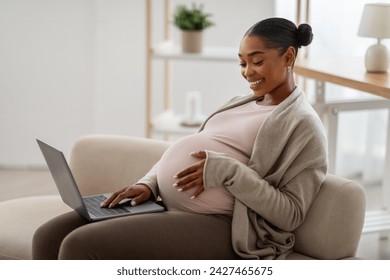 Relaxed african american pregnant young woman using laptop at home, sitting on couch, embracing her big tummy, watching movie or TV show on computer, copy space - Powered by Shutterstock