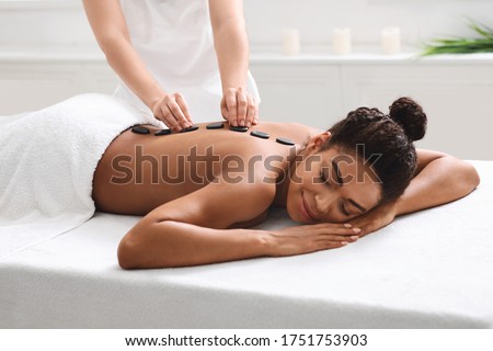 Relaxed african american woman getting hot stone massage at modern spa