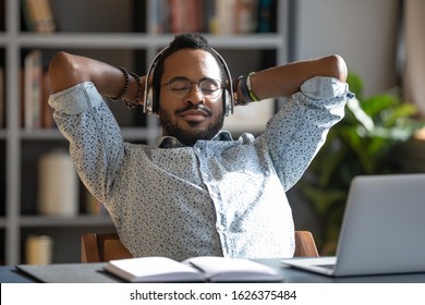 Relaxed African Business Man Wear Wireless Headphones Enjoy Listen Music With Eyes Closed Hand Behind Head Sit At Work Desk, Young Worker Take Break In Office Feel Peace Of Mind Stress Relief Concept