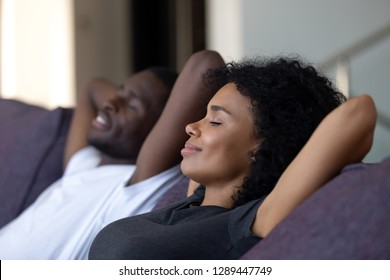 Relaxed african couple enjoying peaceful rest breathing fresh air at home on comfortable couch, happy lazy young black couple having nap leaning on sofa relaxing in living room feel no stress free