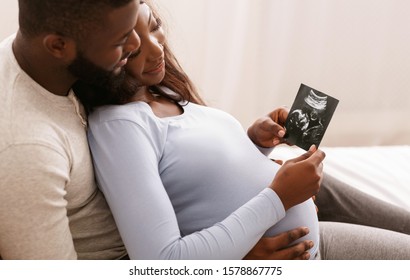 Relaxed African Couple Watching Baby Ultrasound Photo, Lying In Bed At Home, Free Space