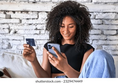 Relaxed afro-haired woman effortlessly shops online with credit card and phone at home. - Shutterstock ID 2329474449
