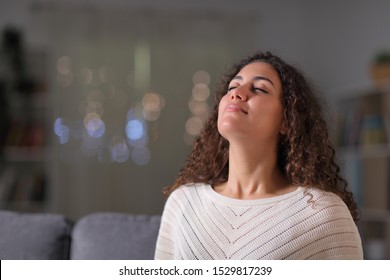 Relaxed Arab Woman Breathing Fresh Air Sitting On A Couch In The Living Room In The Night At Home