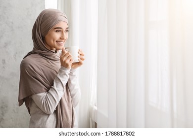 Relaxed Arab Woman In Hijab Enjoying Morning Coffee Near Window At Home, Starting Day With Hot Beverage, Copy Space - Powered by Shutterstock