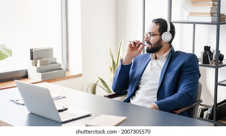 Relaxed Arabian Businessman Manager CEO Boss Listening To Webinar, Online Meeting Conversation In Headphones, Having Break With Music In Earphones.Remote Job At Home Office. Tutor Lecturing E-learning