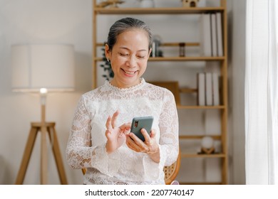 Relaxed asian mature 60s years old woman using smartphone, texting message at home. - Shutterstock ID 2207740147
