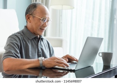 Relaxed Asian Senior Man Using Laptop At His House. Happy Elderly Male Laughing. Retirement