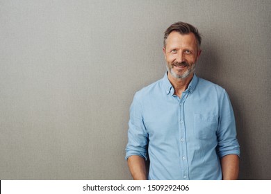 Relaxed attractive smiling middle-aged man with rolled up sleeves posing against a grey studio background with copy space
