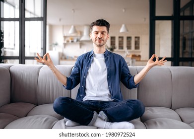 Relaxed attractive young caucasian man, calm pacified guy in casual clothes sits on the sofa in the living room with closed eyes, meditates in the lotus position, relieves stress, resting - Powered by Shutterstock