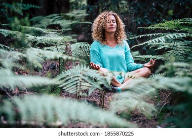 Relaxed beautiful lady do meditation sitting in the middle of nature plant outdoor - people in mindfulness meditate activity enjoying natural outdoors forest in yoga oriental position