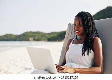 Relaxed Beautiful Young Black Woman Resting On Beach On Sunny Day And Working On Laptop