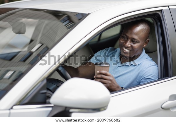 Relaxed black man driver enjoying coffee break\
inside nice white car, sitting at auto front seat, holding paper\
cup with hot tea or coffee, african american guy passing by\
drive-in, buying hot\
drink