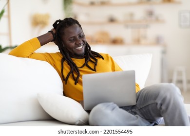 Relaxed Black Man Watching Movies On Laptop While Sitting On Couch At Home, Happy Young African American Male Resting With Computer In Living Room, Enjoying Weekend Leisure, Copy Space