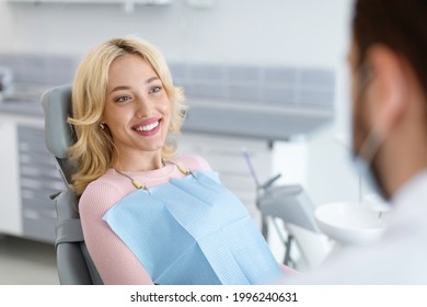 Relaxed blonde woman smiling to her dentist, side view, copy space. Peaceful pretty young lady having conversation with her doctor stomatologist, enjoying modern treatment at new dental clinic