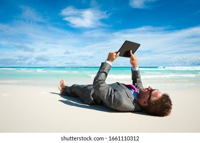 Relaxed businessman lying in a suit using his tablet computer on the shore of a tropical beach - Shutterstock ID 1661110312