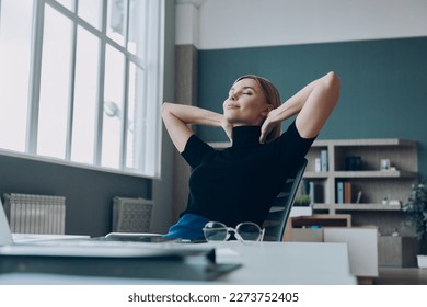 Relaxed businesswoman holding hands behind head while sitting at her working place in office - Powered by Shutterstock