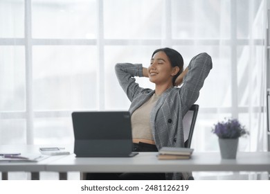 Relaxed businesswoman stretching at her desk in a modern office environment. Successful and confident professional taking a break. - Powered by Shutterstock