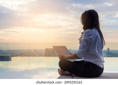 Relaxed calm asian woman sitting on the floor with crossed legs, using laptop, resting looking away sit at pool on skyscraper,enjoy fresh conditioned air, relief peace of mind concept chill at working - Powered by Shutterstock