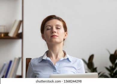 Relaxed calm business woman take deep breath of fresh air resting in chair lounge with eyes closed at work in office, serene happy female employee meditate feeling no stress free relief at workplace