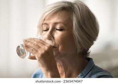 Relaxed calm elder retired woman drinking natural fresh water with closed eyes, holding transparent clear glass, keeping healthy nutrition, diet, hydration balance for dry skin care, metabolism - Powered by Shutterstock