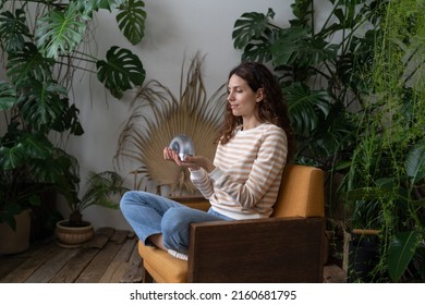 Relaxed Calm Woman Playing With Spring Toy For Stress Relief Sit Crossed Legs In Armchair. Female Relieve Stressful Tension With Stretchable Spring Has Break From Work At Home Office In Indoor Garden