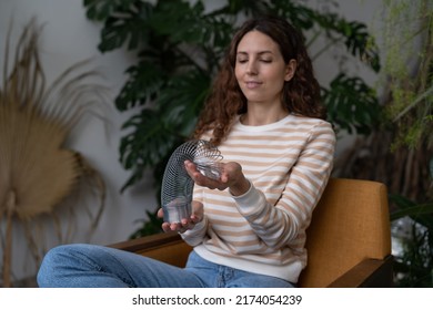 Relaxed Calm Woman Playing With Spring Toy For Stress Relief Sit Crossed Legs In Armchair. Female Relieve Stressful Tension With Stretchable Spring Has Break From Work At Home Office In Indoor Garden