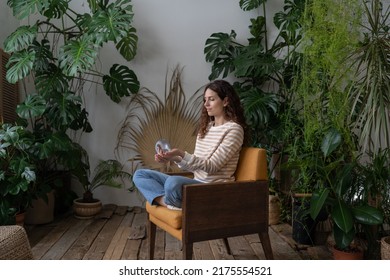 Relaxed Calm Woman Playing With Spring Toy For Stress Relief Sit Crossed Legs In Armchair. Female Relieve Stressful Tension With Stretchable Spring Has Break From Work At Home Office In Indoor Garden