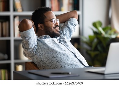 Relaxed calm young african businessman resting looking away sit at desk with laptop hands behind head, satisfied office employee take break feel stress relief peace of mind concept chill at work