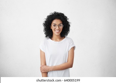 Relaxed carefree smiling young woman wearing white t-shirt and glasses having positive cheerful expression on her face, rejoicing at her leisure time, spending day at home. Horizontal studio shot - Powered by Shutterstock