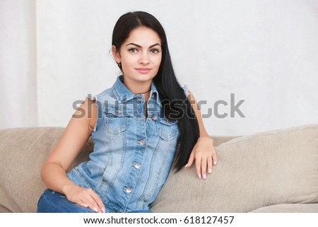 Relaxed casual brunette in blue cardigan and In blue jeans sits on the couch in bright living room