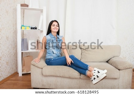 Relaxed casual brunette in blue cardigan and In blue jeans sits on the couch in bright living room