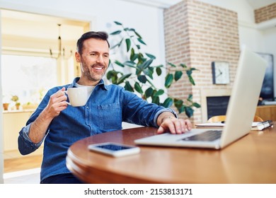 Relaxed Casual Man Working On Laptop Drinking Coffee At Home