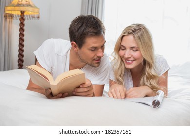 Relaxed Casual Young Couple Reading Books In Bed At Home