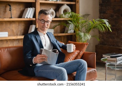 Relaxed caucasian mature middle-aged businessman freelancer ceo boss employee reading business journal while having breakfast drinking coffee at office before working day - Powered by Shutterstock