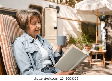 Relaxed caucasian senior old elderly woman grandmother granny reading book, learning near trailer porch, traveling by motor home, caravanning by camper van - Powered by Shutterstock